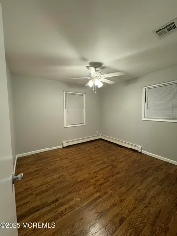 a view of an empty room with wooden floor and fan