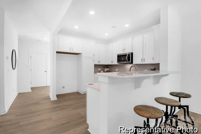 a kitchen with stainless steel appliances granite countertop a stove a refrigerator a microwave oven a dining table and chairs with wooden floor