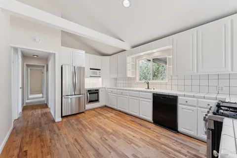 a kitchen with stainless steel appliances granite countertop a refrigerator a sink dishwasher a stove with wooden floors and cabinets