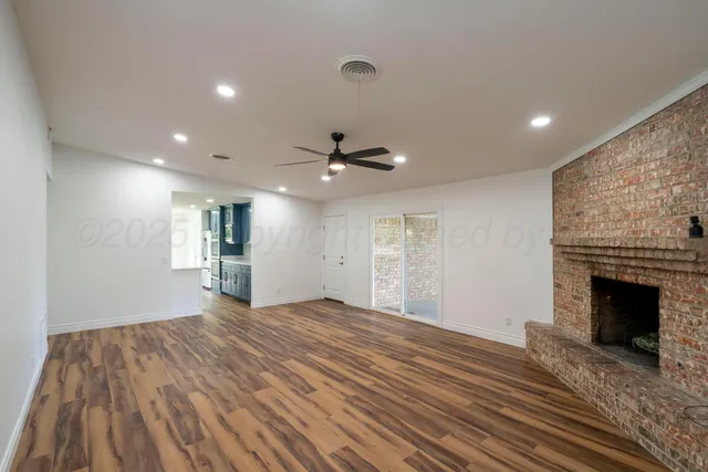 a view of an empty room with wooden floor fireplace and a window
