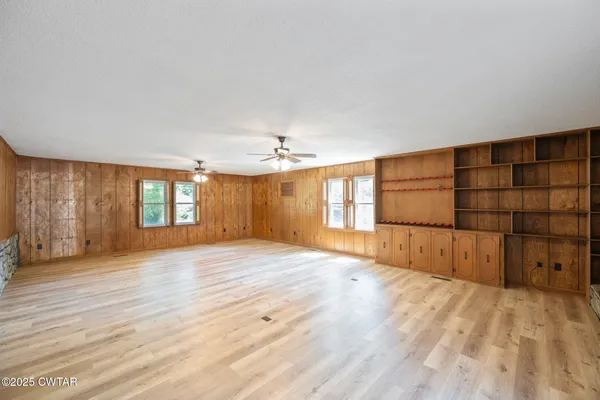 an empty room with wooden floor chandelier fan and windows