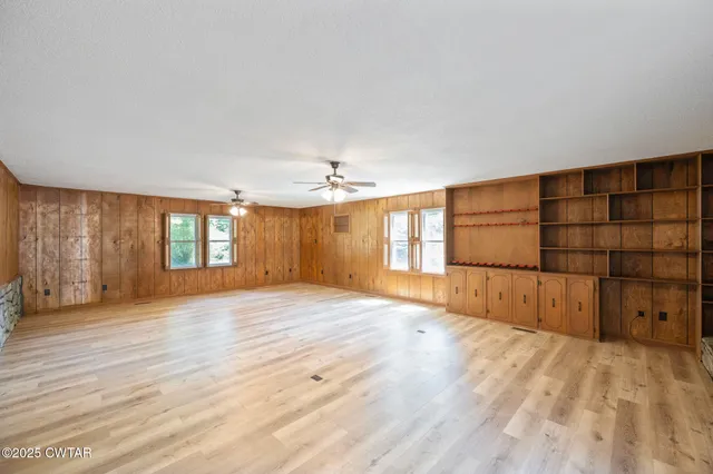 an empty room with wooden floor chandelier fan and windows