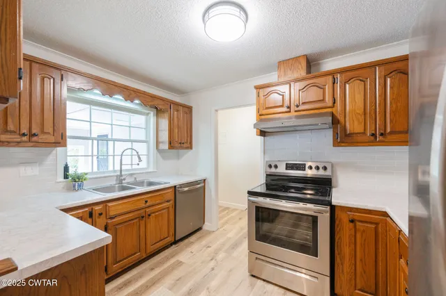 a large living room with stainless steel appliances granite countertop a sink dishwasher stove and wooden cabinets