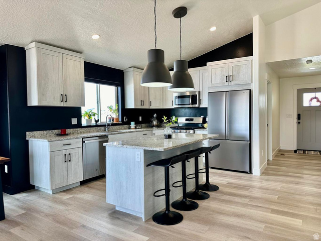 4349 Half Mile Road East Enoch, UT 84721 - Photo 9 of 36 Kitchen with light stone countertops, stainless steel appliances, a kitchen bar, and light wood-style flooring