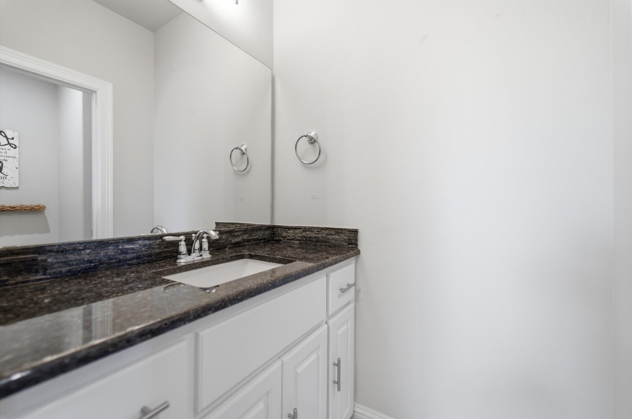 23722 Thortons Park Lane Spring, TX 77389 - Photo 37 of 48 This photo shows a modern bathroom with a sleek black granite countertop, white cabinetry, and a large mirror, creating a clean and elegant look.