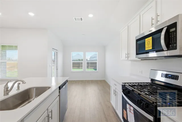 a kitchen with stainless steel appliances a stove a sink a microwave cabinets and a wooden floor