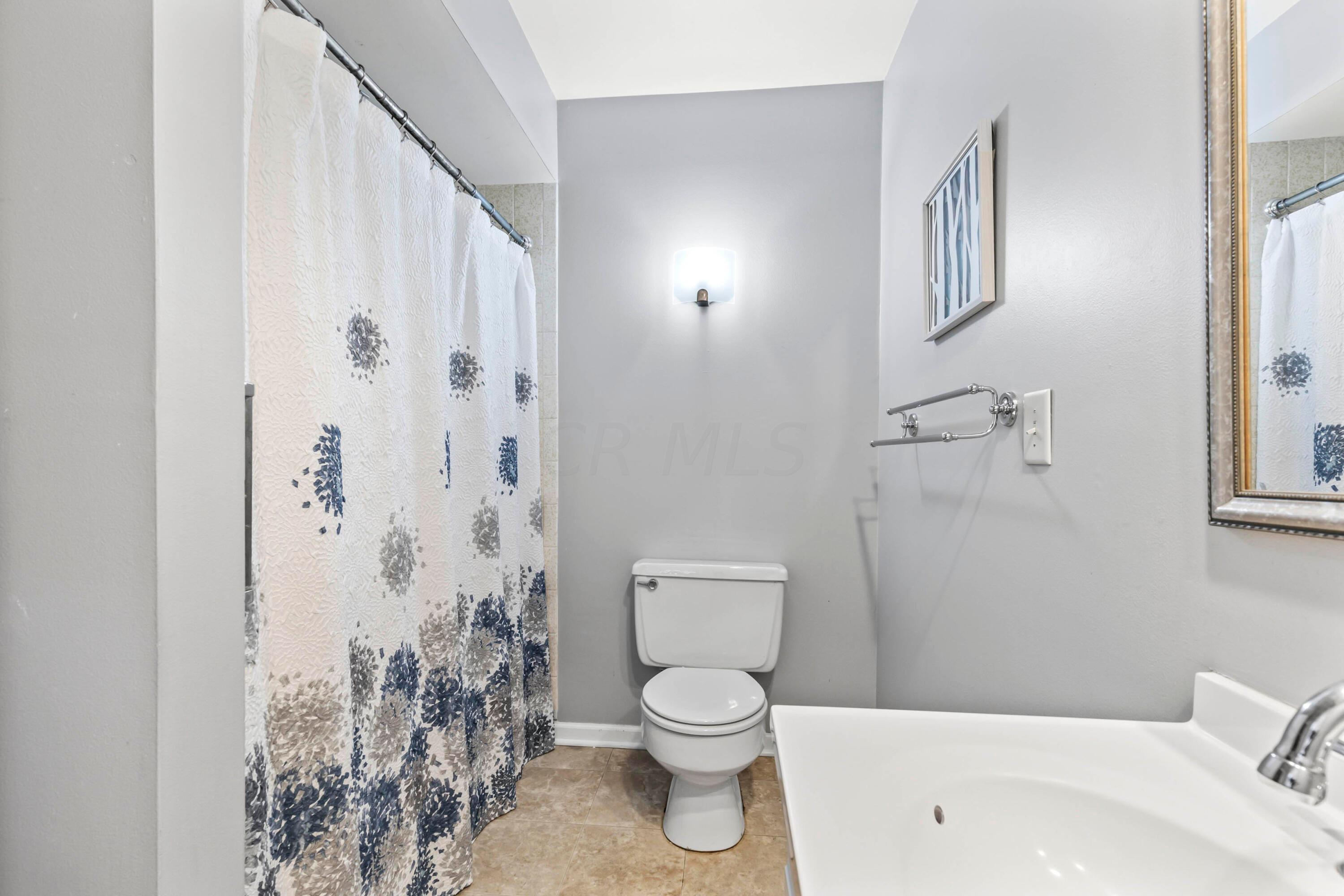 7020 Rieber Street Columbus, OH 43085 - Photo 27 of 40 • New neutral vinyl flooring ~ 2006 • Grey painted walls • Enclosed vanity with single bowl, cultured marble sinktop • Ceiling exhaust • Tub/shower combination with ceramic tile surround • Wall mounted light • 2” blinds