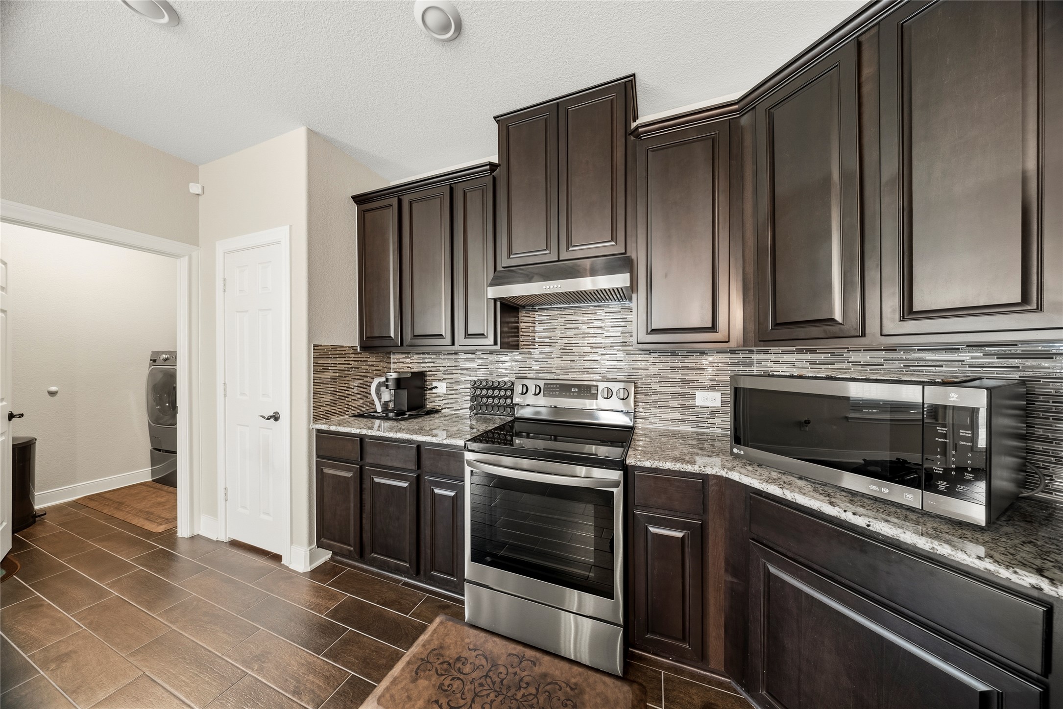 105 West Point Way Elgin, TX 78621 - Photo 6 of 27 Kitchen featuring dark wood cabinetry, granite countertops, a tile backsplash, and stainless steel appliances