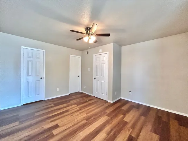 an empty room with wooden floor fan and windows