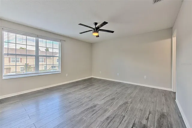 an empty room with wooden floor fan and windows