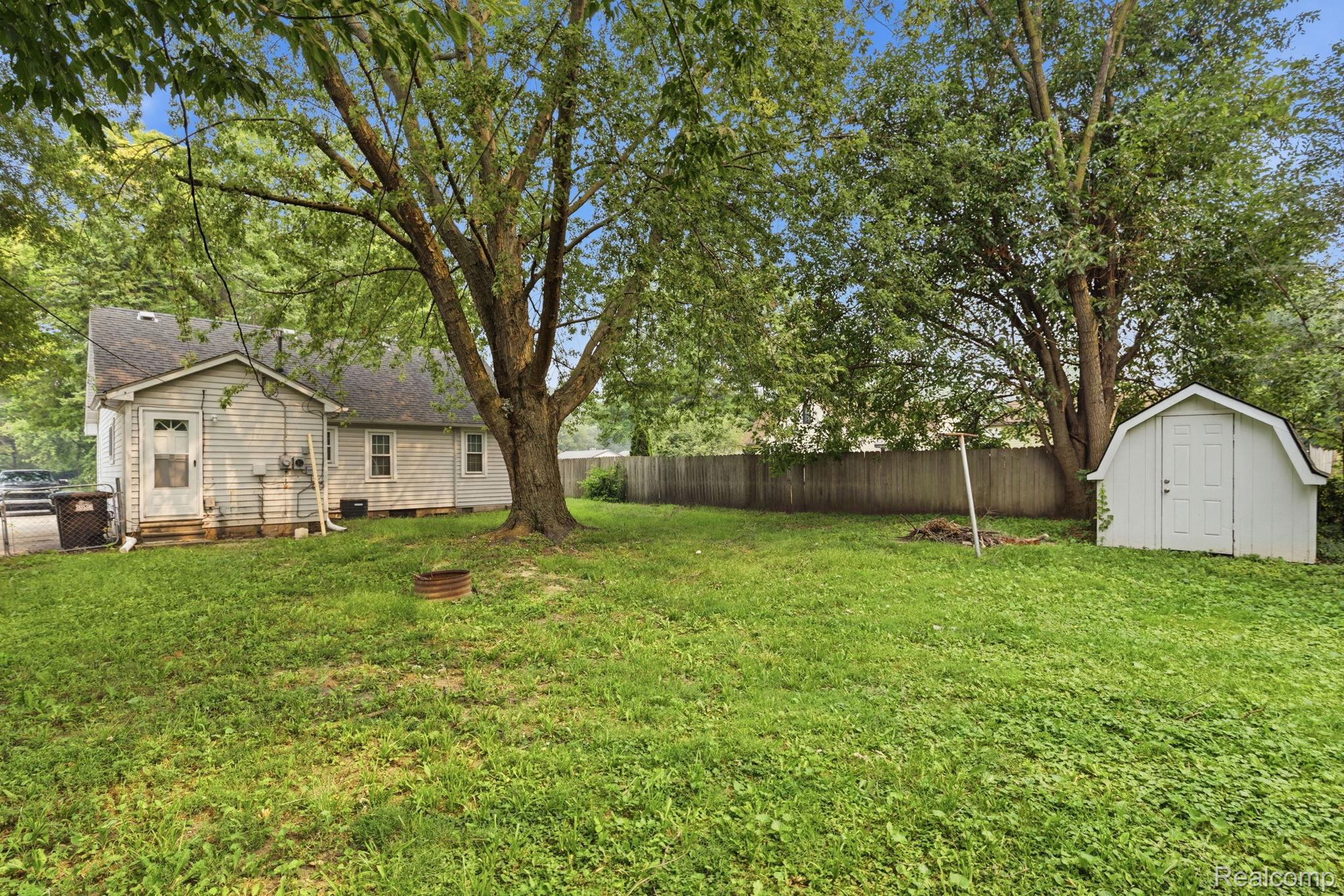 5852 Beech Daly Road Taylor, MI 48180 - Photo 27 of 29 Expansive backyard featuring a manicured lawn, a large mature tree, a white storage shed with a gambrel roof, and a wood privacy fence
