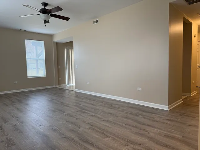 an empty room with wooden floor fan and windows