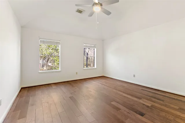 an empty room with wooden floor chandelier fan and windows