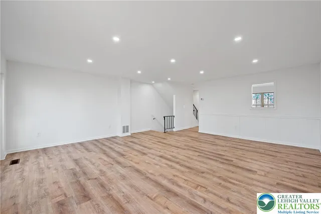 a view of an empty room with wooden floor and fan