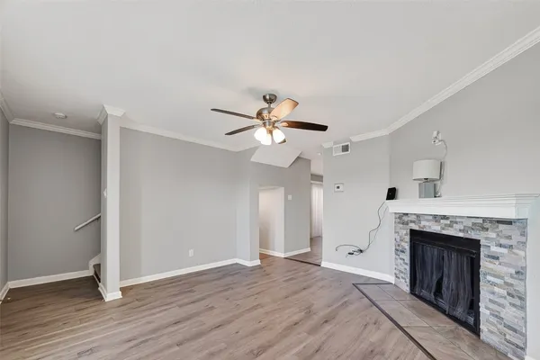 an empty room with wooden floor a ceiling fan a fireplace and windows