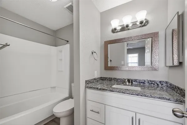 a bathroom with a granite countertop sink a toilet a mirror a vanity a bathtub and shower