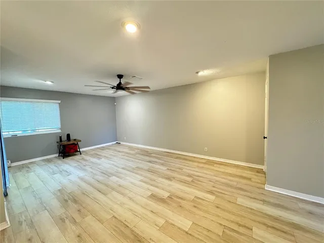 an empty room with wooden floor fan and windows