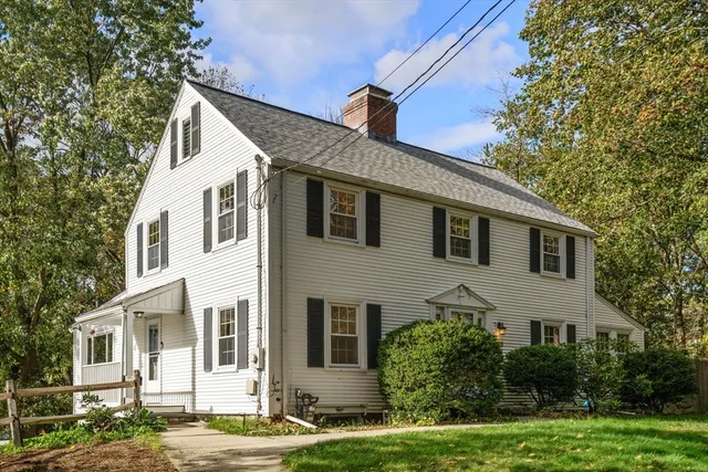 a view of a white house next to a yard with plants and trees