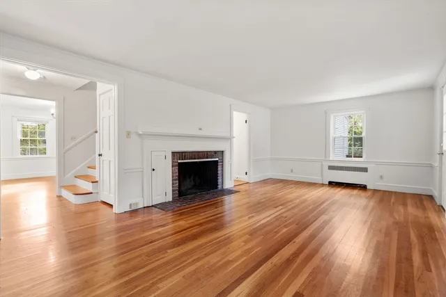 an empty room with wooden floor fireplace and windows
