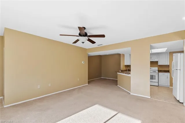 a view of a livingroom with a ceiling fan & kitchen space
