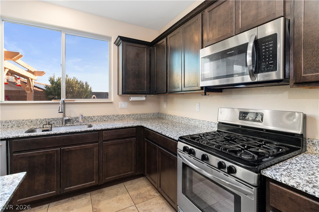 2079 Port Royal Drive Laughlin, NV 89029 - Photo 17 of 86 Kitchen featuring appliances with stainless steel finishes, dark brown cabinetry, light stone countertops, and light tile patterned floors
