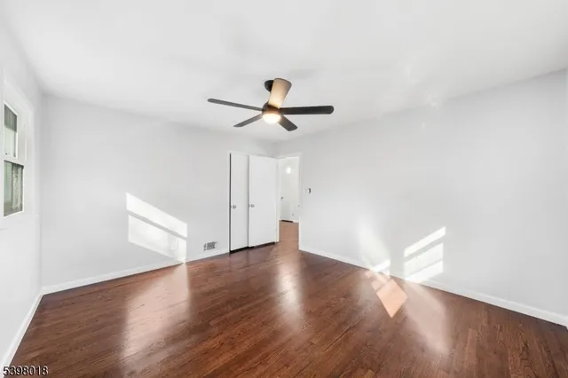 an empty room with wooden floor ceiling fan and window