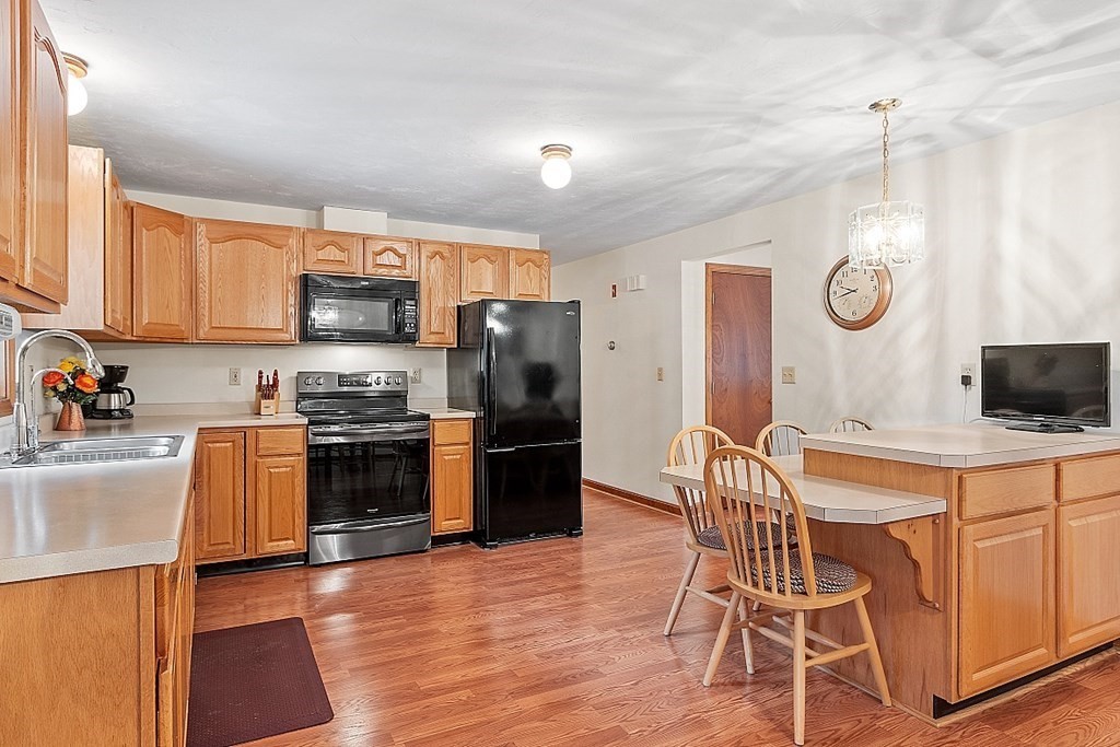 252 Great Road Shirley, MA 01464 - Photo 17 of 42 a kitchen with stainless steel appliances a stove a sink a refrigerator cabinets and a dining table with wooden floor