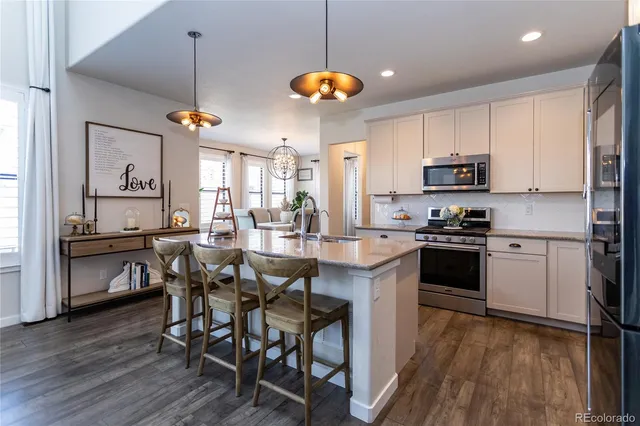a kitchen with stainless steel appliances kitchen island granite countertop a dining table chairs stove and white cabinets