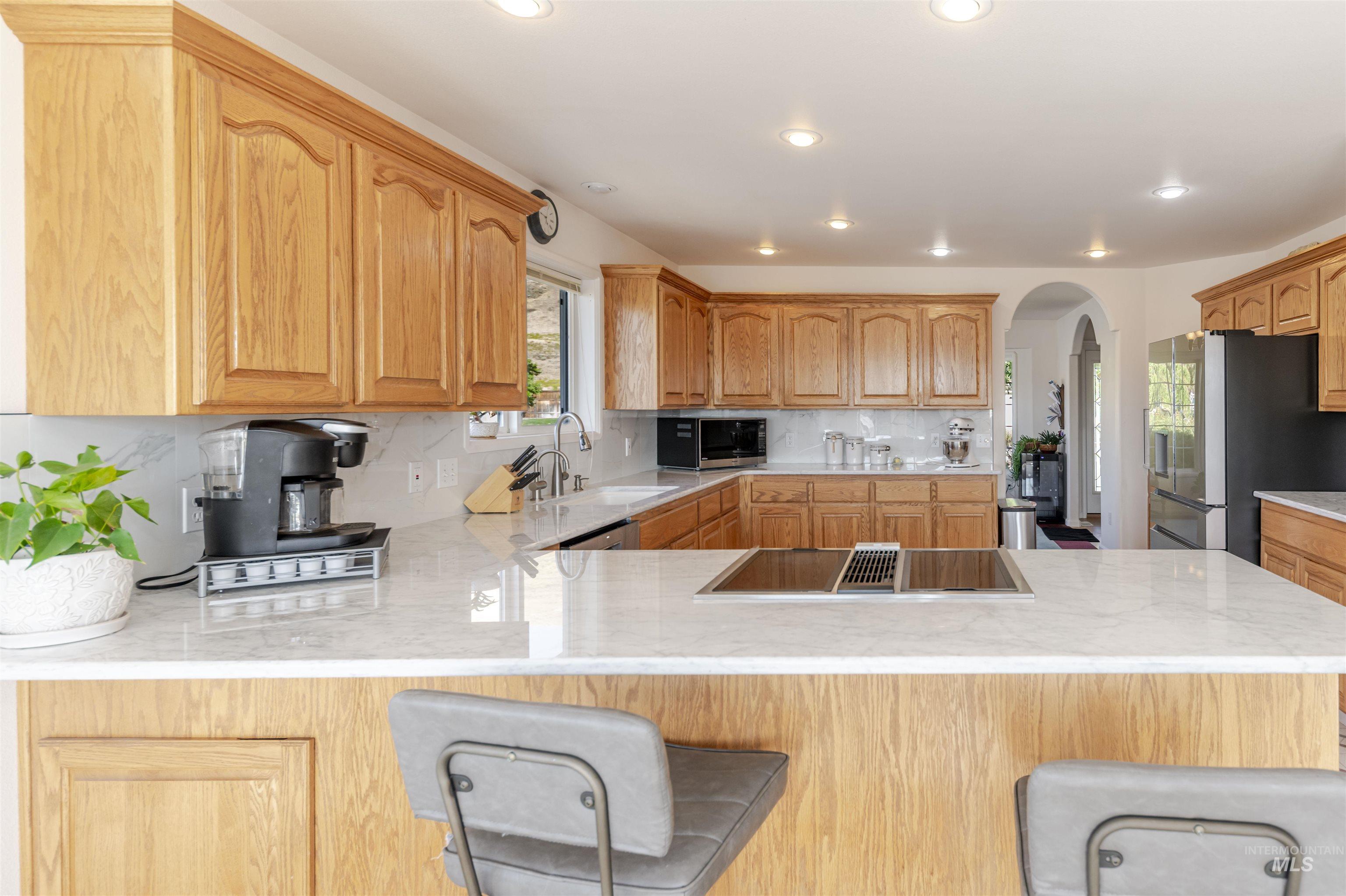 331 Reservoir Drive Lewiston, ID 83501 - Photo 9 of 42 Kitchen featuring a breakfast bar, arched walkways, stainless steel appliances, backsplash, and light stone countertops