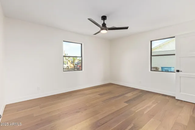 an empty room with wooden floor ceiling fan and windows