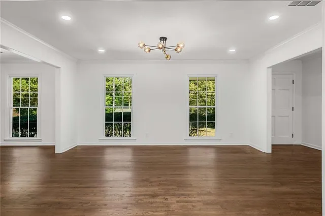 an empty room with wooden floor chandelier and windows