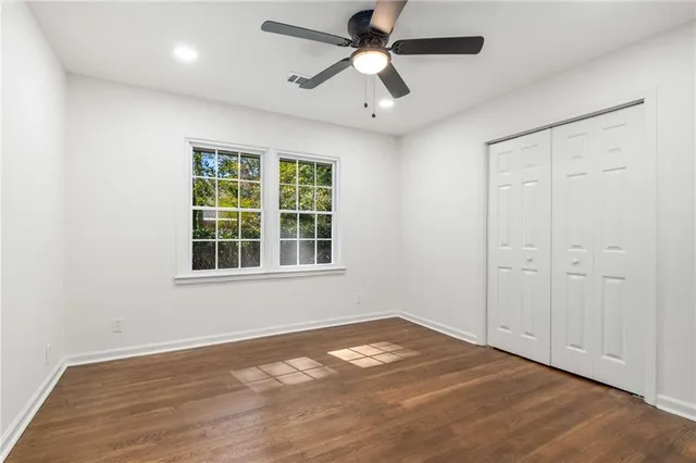an empty room with wooden floor chandelier fan and windows