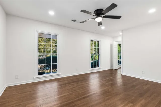 an empty room with wooden floor chandelier fan and windows