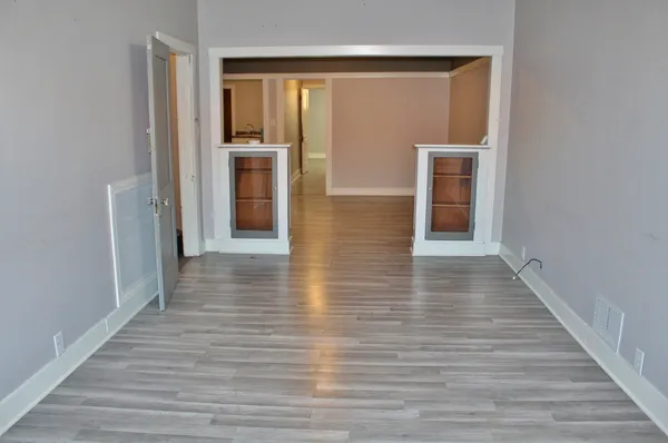 a view of a hallway to an empty room with wooden floor and a window