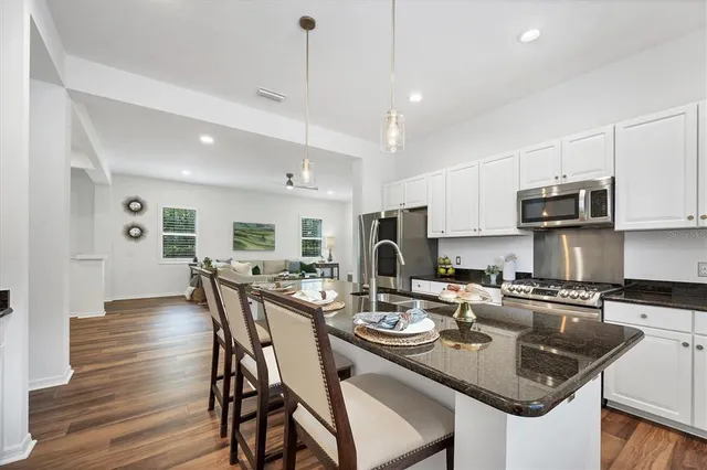 a kitchen with stainless steel appliances granite countertop a sink a stove a dining table and chairs with wooden floor