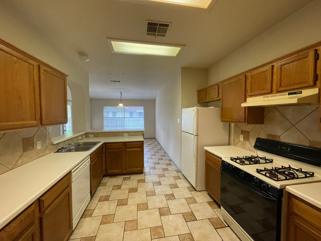 1212 Knoll Ridge Drive Cedar Park, TX 78613 - Photo 5 of 10 Kitchen featuring white appliances, decorative backsplash, brown cabinetry, light countertops, and under cabinet range hood
