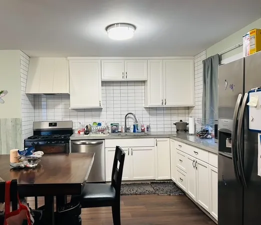 a kitchen with stainless steel appliances granite countertop a sink a stove a refrigerator cabinets and a dining table with wooden floor