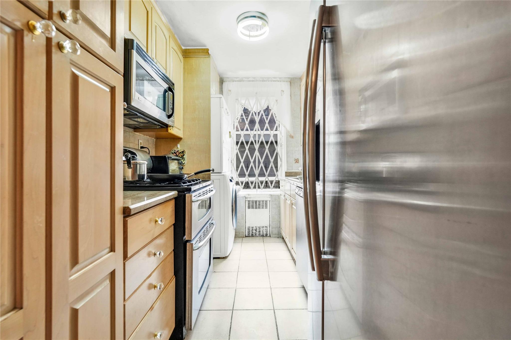 42-25 80th Street, Unit 1F Queens, NY 11373 - Photo 13 of 27 Kitchen with radiator heating unit, light countertops, light tile patterned flooring, and appliances with stainless steel finishes