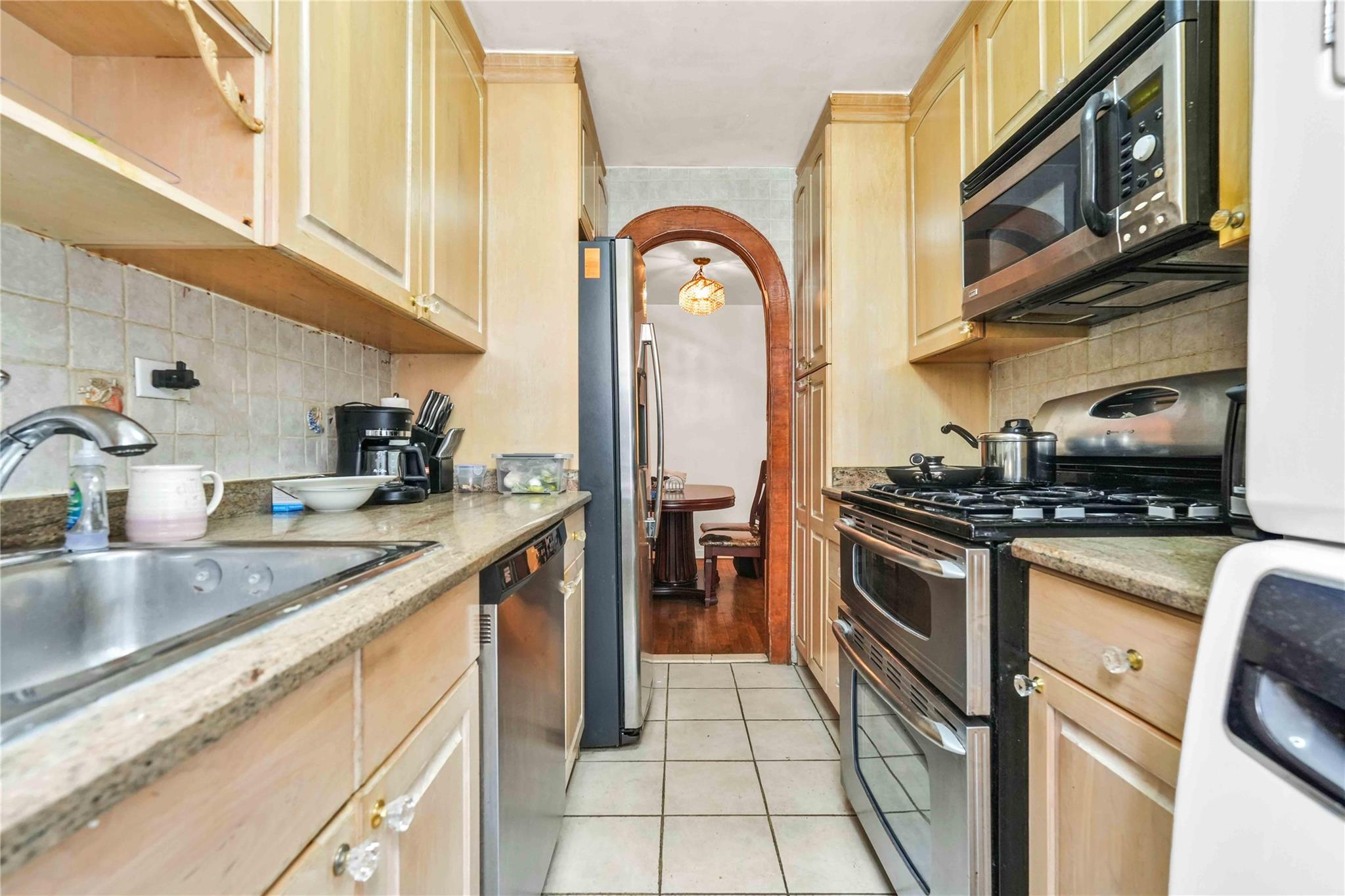 42-25 80th Street, Unit 1F Queens, NY 11373 - Photo 17 of 27 Kitchen with light tile patterned floors, light brown cabinets, appliances with stainless steel finishes, and decorative backsplash