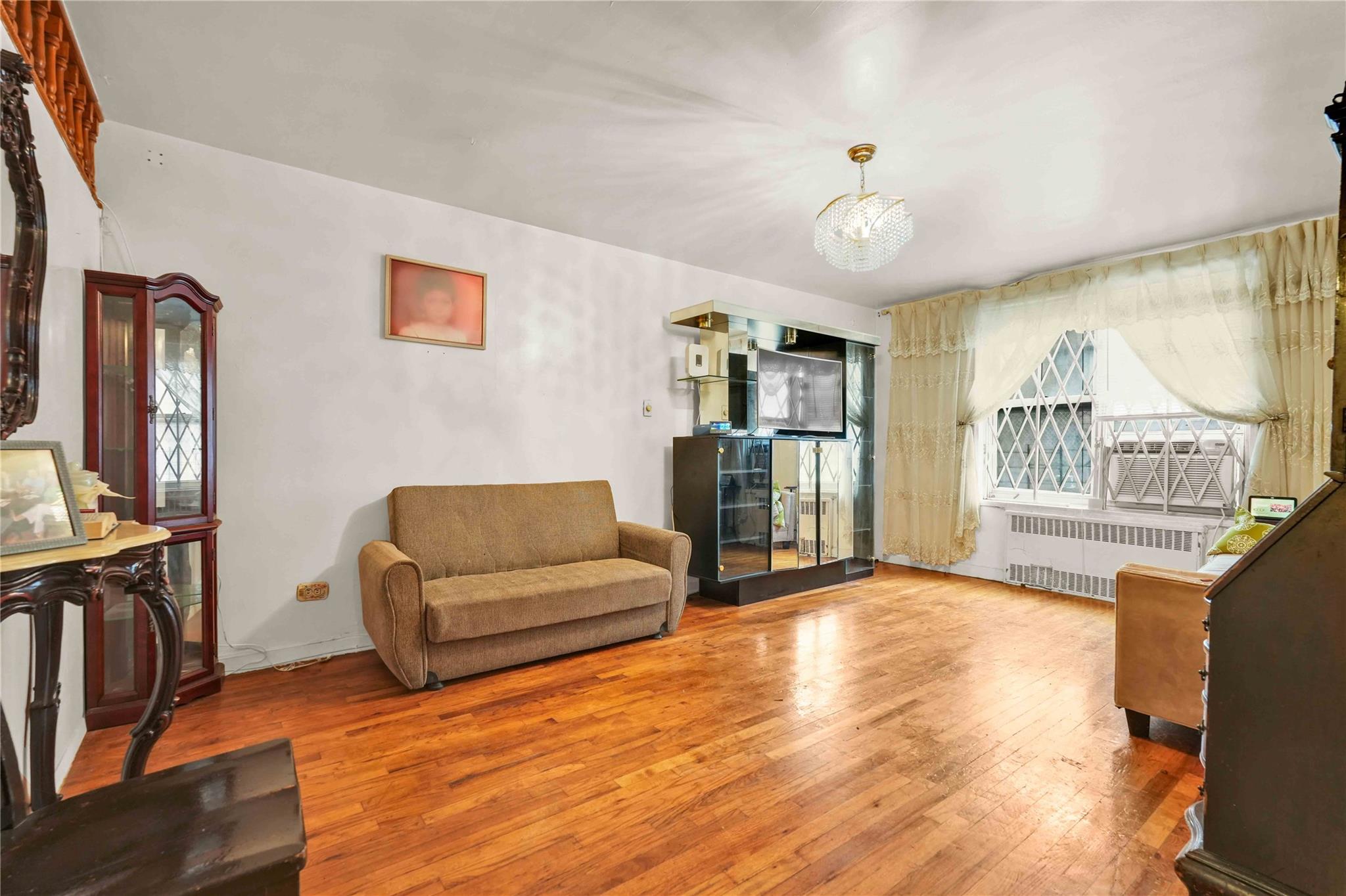 42-25 80th Street, Unit 1F Queens, NY 11373 - Photo 7 of 27 Living area featuring radiator heating unit, hardwood / wood-style flooring, and a chandelier