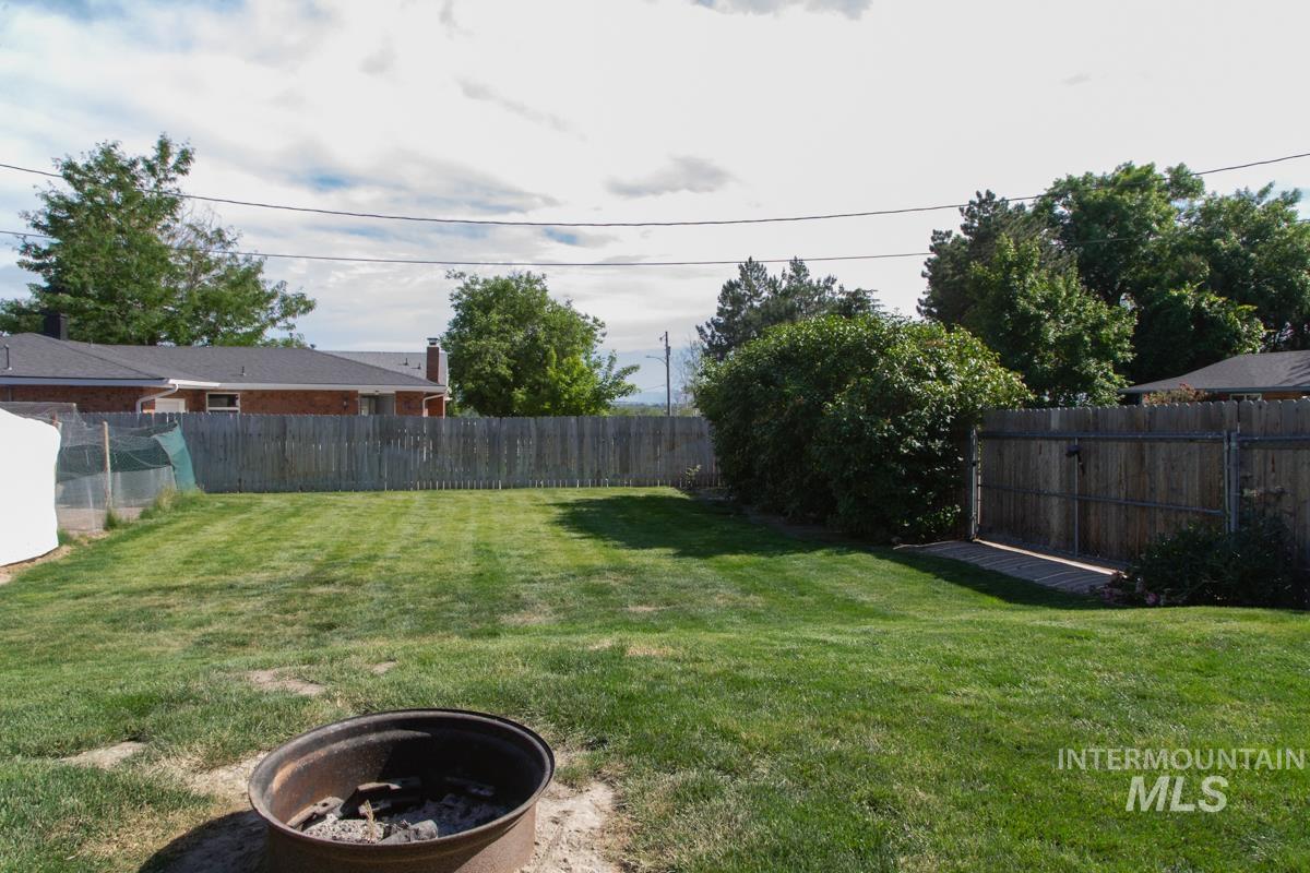 1404 Rochester Street Caldwell, ID 83605 - Photo 25 of 29 Expansive rear yard featuring a large grass area, wood privacy fencing, mature perimeter bushes, and a metal fire pit