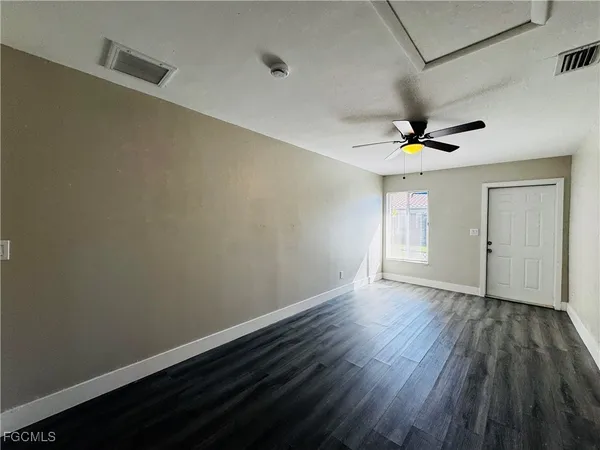an empty room with wooden floor chandelier fan and windows