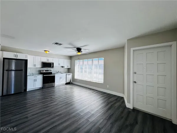 an empty room with wooden floor kitchen view and a window