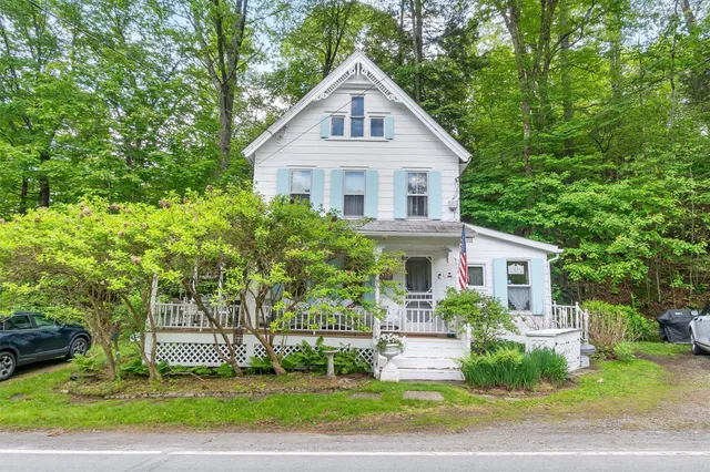 a view of a white house next to a yard with big trees