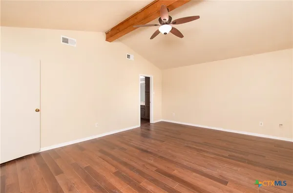 an empty room with wooden floor fan and windows
