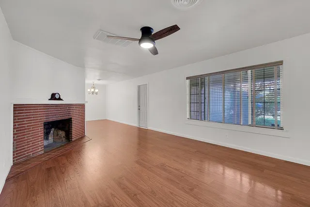 a view of an empty room with wooden floor fireplace and a window