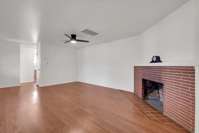 a view of an empty room with wooden floor a fireplace and a window