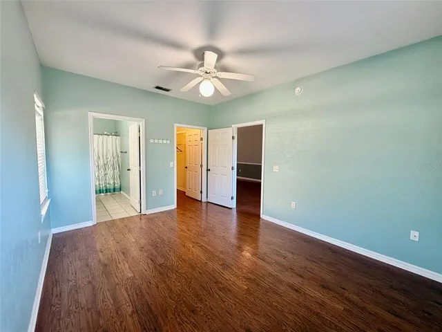 a view of an empty room with wooden floor and a ceiling fan