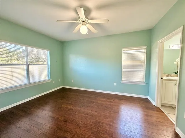 an empty room with wooden floor fan and windows