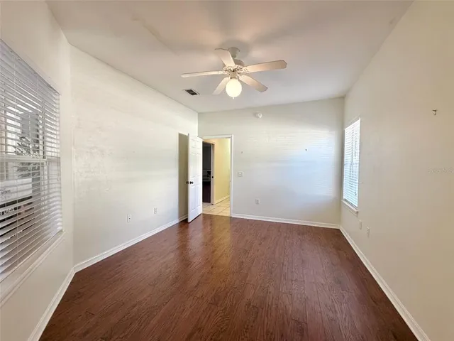 an empty room with wooden floor fan and windows